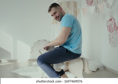 Adult Autistic Man Riding A Toy Horse In Child Room, Smiling Man Wearing Casual Clothes Riding On Toy Wooden Horse