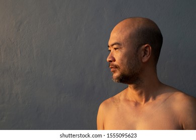 adult bald beard 40s Japanese man topless profile portrait with dark grey blue concrete wall background 