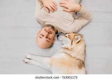 Adult Bald Man With Husky Puppy Sleeping On Floor. Owner With Pet Together At Home. Kind And Soulful Emotions. Lovely Dog Resting With Young Male. Guy With Beloved Domestic Animal Hugging Each Other.