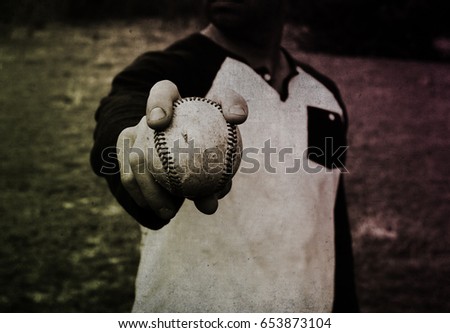 Adult ball player holding game ball in hand, can see closeup the retro style of hardball image.  Baseball pitcher getting ready to throw fastball in outside fun practice.  