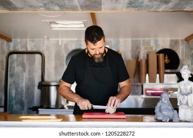 Adult Bearded Man In Black Apron Slicing Fish Liver At Counter In Street Food Truck