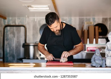 Adult Bearded Man In Black Apron Slicing Fish Liver At Counter In Street Food Truck