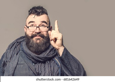Adult bearded man with glasses and scarf showing forefinger up on a brown background. Toned