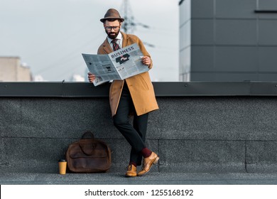 adult bearded man standing with crossed legs and reading business newspaper on roof - Powered by Shutterstock