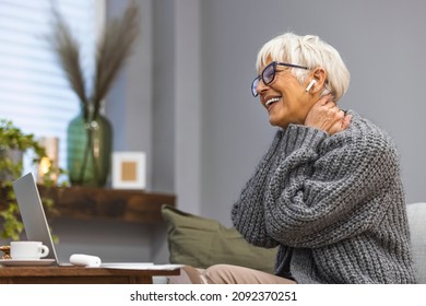 An Adult Beautiful Woman In A Grey Sweater And Glasses Sitting At Home On A Sofa With A Mug In Her Hands In Front Of A Laptop Screen . Women At Home During Pandemic Isolation Have Conference Call