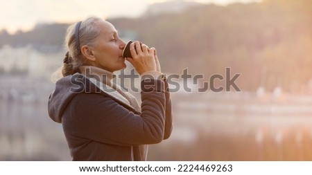 An adult beautiful woman holds a glass of aromatic coffee in her hands and enjoys the taste and atmosphere at sunset, views of the city and the river.