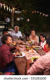 Adult Black Family Enjoy Dinner Together In Garden, Vertical