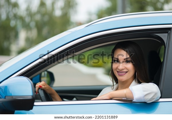 Adult black-haired woman driver sits in\
blue car. Stylish businesswoman enjoys successful life smiling.\
Happy lady grimaces in leather cabin\
closeup