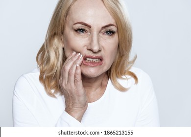 An Adult Blonde Holds On To A Tooth And Suffers From Severe Pain In Her Teeth. The Girl Has Clenched Her Jaw And Feels Severe Pain In Her Teeth.