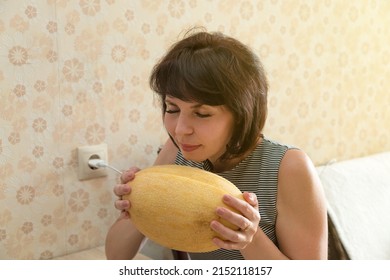 An Adult Brunette Woman Holds Large Yellow Melon Inhaling Pleasant Aroma.