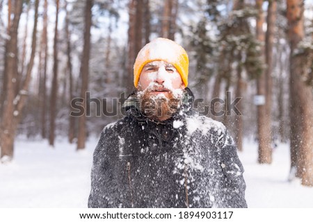 An adult brutal man with a beard in a winter forest all face in the snow, frozen, unhappy with the cold