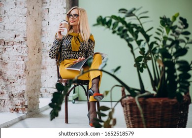 Adult business woman sitting in chair drinking coffee and reading magazine