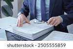 Adult businessman or auditor examining documents with magnifying glass. Professional in a suit scrutinizes financial reports, detail-focused work concept