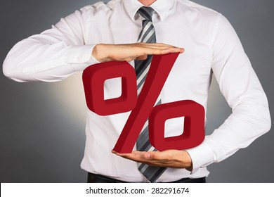 Adult businessman holding 3 D percent sign, isolated on dark background. 