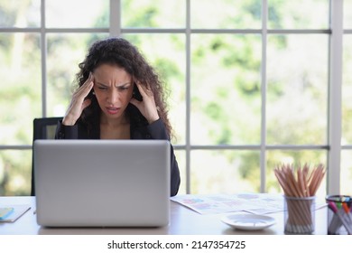 Adult businesswoman sitting and touching her head and looking at computer in office after bad news business failure or get fired and feeling discouraged, distraught and hopeless in modern office