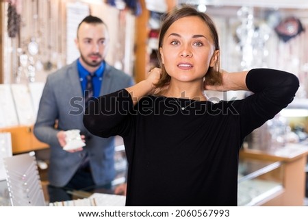 Adult buyer woman choosing chainlet and pendants in the jewelry store.