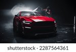Adult Car Washer in Uniform Washing a Red Performance Car with a High Pressure Cleaner. Cleaning Technician Working on a Stylish American Car in a Dark Room. Commercial Studio Footage for Advertising