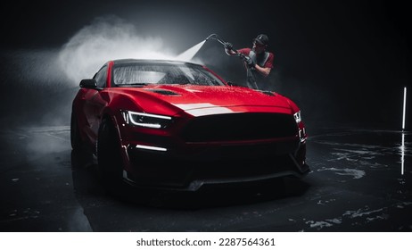 Adult Car Washer in Uniform Washing a Red Performance Car with a High Pressure Cleaner. Cleaning Technician Working on a Stylish American Car in a Dark Room. Commercial Studio Footage for Advertising