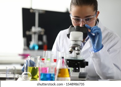Química adulta caucasiana de beleza em óculos de proteção olhando para o microscópio contra o fundo do laboratório de química. Conceito de processamento de análise médica