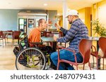 Adult caucasian and casual man feeding a colleague with disability in a coworking cafeteria