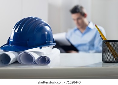 adult caucasian male architect examining documents. Focus on blueprints and hardhat in foreground. Horizontal shape, front view