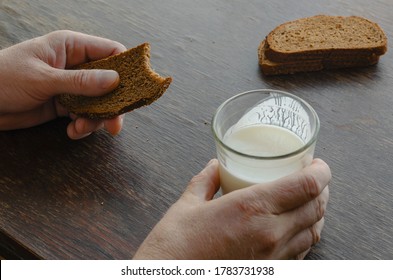 Adult Caucasian Male Eating Kefir With Rye Bread. One Hand Holds Half-empty Glass Of Kefir. Another Bitten Slice Of Rye Bread. Simple Healthy Food. Top View At An Angle.