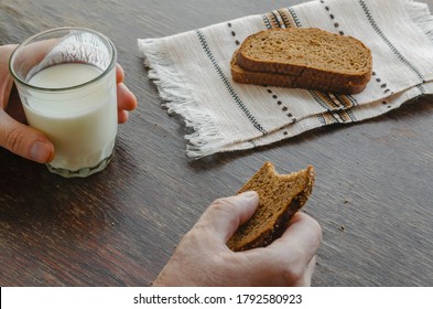 Adult Caucasian Male Eating Kefir With Rye Bread. One Hand Holds Half-empty Glass Of Kefir. Another Bitten Slice Of Rye Bread. Simple Healthy Food. Top View At An Angle.