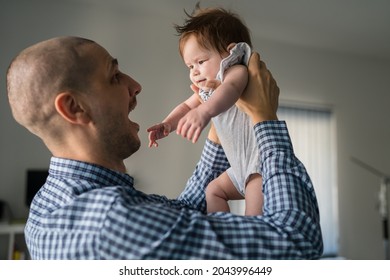 Adult Caucasian Man Father Wearing Blue Shirt Holding His Small Five Months Old Baby Girl Child While Standing By The Window At Home Fatherhood And Parenting Concept Father's Day Real People Side View