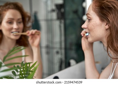 Adult caucasian woman brushing teeth in the bathroom - Powered by Shutterstock