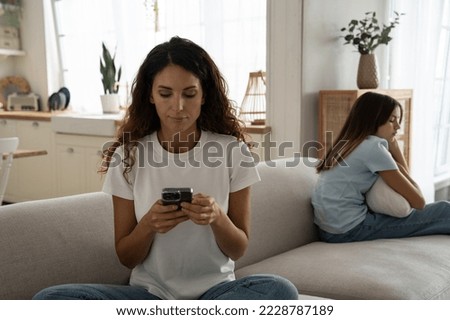 Adult Caucasian woman with mobile phone in hand sits on sofa on other side of depressed daughter. Caring mother calls child psychologist for teenage girl after showing signs stress and peer problems