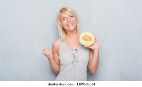 Adult Caucasian Woman Over Grunge Grey Wall Eating Cantaloupe Melon Screaming Proud And Celebrating Victory And Success Very Excited, Cheering Emotion