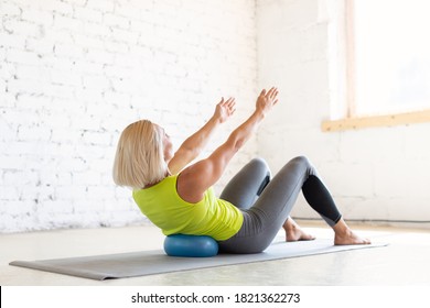 Adult caucasian woman practice pilates indoor. Seated rolls up with small fit ball on a mat, abs and back drill, in loft white studio, selective focus. Workout, stretching, fitness, trainer, recovery