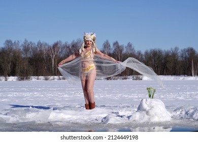 An Adult Cheerful Woman In Faun Costume With Horns With Snowdrops On The Edge Of An Ice Hole With Cold Water On Sunny Winter Day.