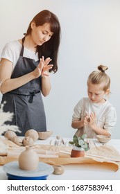 Adult And Child In Aprons Are Sculpting Together Behind A Table In Potter Studio