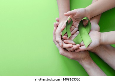 Adult And Child Hands Holding Lime Green Ribbon On Green Background, Children Mental Health Awareness And Lymphoma Awareness, World Mental Health Day, World Kidney Day, Organ Donation