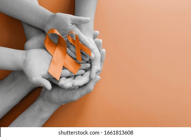 Adult And Child Hands Holding Orange Ribbons,  Leukemia Cancer And Multiple Sclerosis, COPD And ADHD Awareness, World Kidney Day