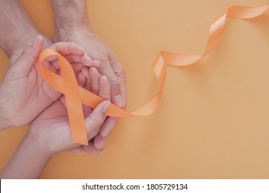 Adult And Child Hands Holding Orange Ribbons,  Leukemia Cancer And Multiple Sclerosis, COPD And ADHD Awareness, World Kidney Day