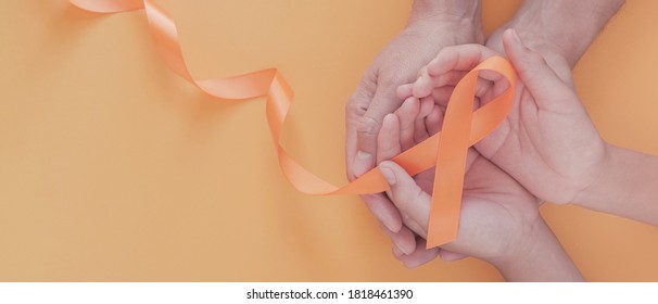 Adult And Child Hands Holding Orange Ribbons,  Leukemia Cancer And Multiple Sclerosis, COPD And ADHD Awareness, World Kidney Day