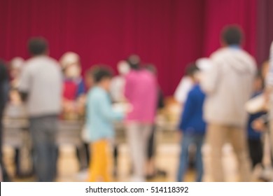 Adult And Child Lined Up Waiting For Food In School Meeting Room