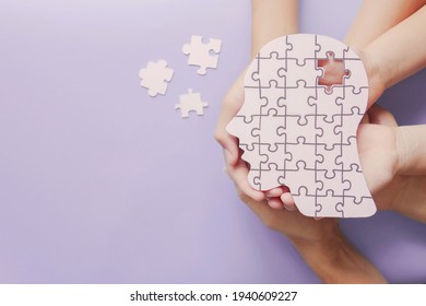 Adult and children hands holding brain with puzzle paper cutout, autism, memory loss, dementia, epilepsy and alzheimer awareness, world mental health day, world Parkinson day concept