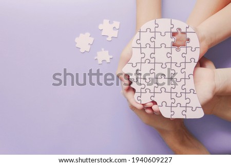 Adult and children hands holding brain with puzzle paper cutout, autism, memory loss, dementia, epilepsy and alzheimer awareness, world mental health day, world Parkinson day concept
