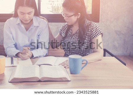 A adult Christian  woman  praying for her your woman friend with the open bible on wooden table at church prayer room to encourage and support him in his problem and spiritual growth.