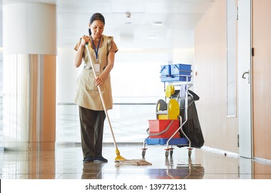 Adult cleaner maid woman with mop and uniform cleaning corridor pass or hall floor of business building