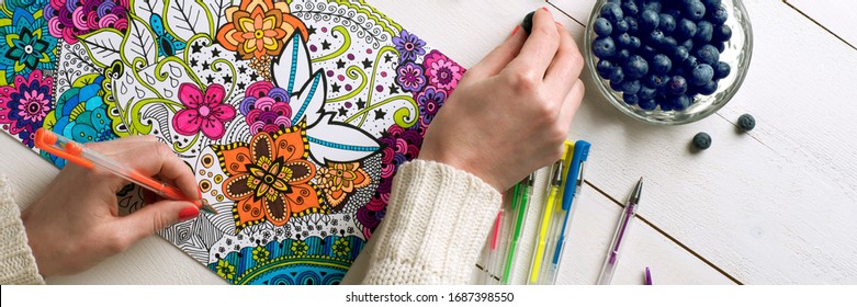 Adult coloring book, stress relieving trend. Art therapy, mental health, creativity and mindfulness concept. Flat lay close up on woman hands coloring an adult coloring book web banner.