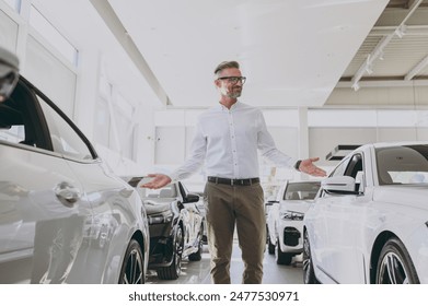 Adult confident rich man customer male buyer client wear classic shirt point hands on cars choose auto want to buy new automobile in showroom vehicle salon dealership store motor show. Sales concept
