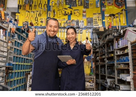 Adult couple of entrepreneurs, man and woman, with uniform working happily in business full of merchandise.