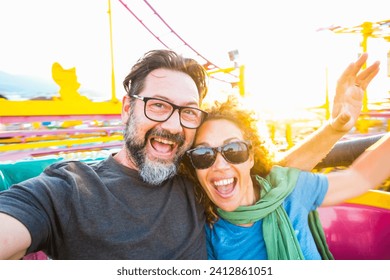 Adult couple have fun together on a roller coaster in amusement park taking selfie picture with the phone. People enjoying holiday lifestyle. Mature man and woman enjoy time outdoor leisure activity - Powered by Shutterstock