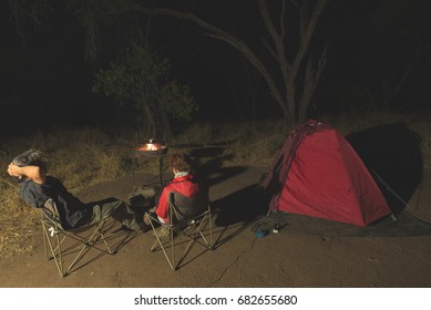 Adult couple relaxing in camping site by night. Adventure in National Park, South Africa. Burning camp fire and tent in the background. Toned image.
 - Powered by Shutterstock