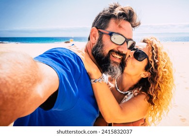 Adult couple of tourist take selfie picture at the beach with sand and ocean in background. People enjoy and have fun using phone camera in outdoor leisure activity - Powered by Shutterstock