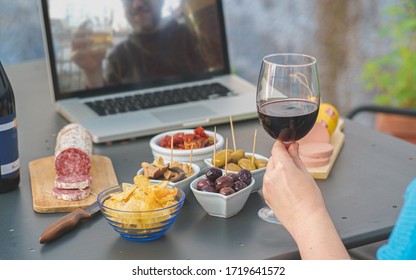 Adult couples clinking online with beer and wine making a quarantine happy hour toast via internet video call. Alcohol and aperitif lifestyle concept. focus on the wineglass.
